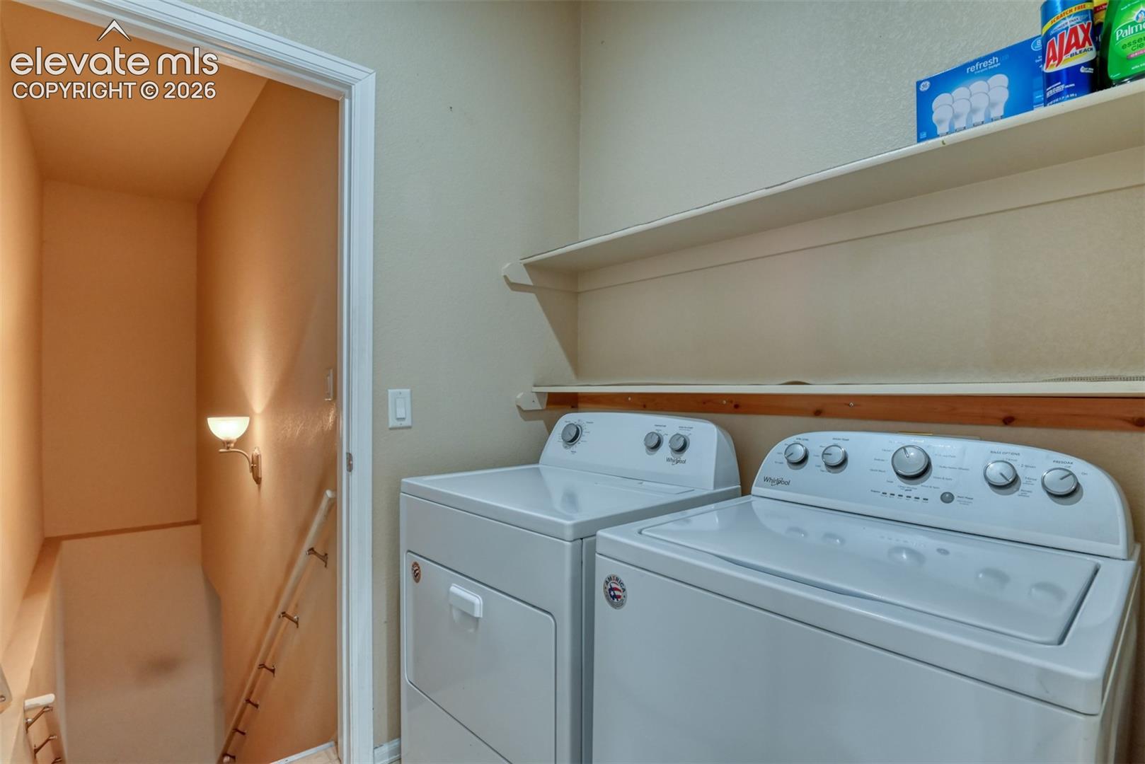 Laundry area featuring built-in shelving, white high-capacity appliances, and a wall-mounted light fixture