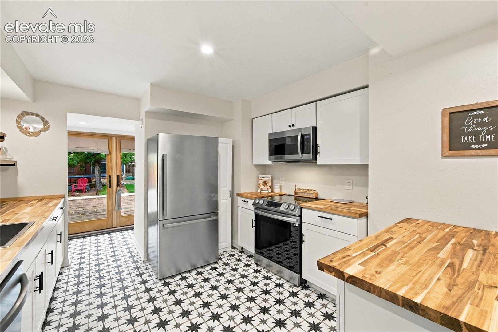 Kitchen featuring white shaker-style cabinetry, wood-finish countertops, stainless steel appliances, patterned tile flooring, and double glass-paned exterior doors