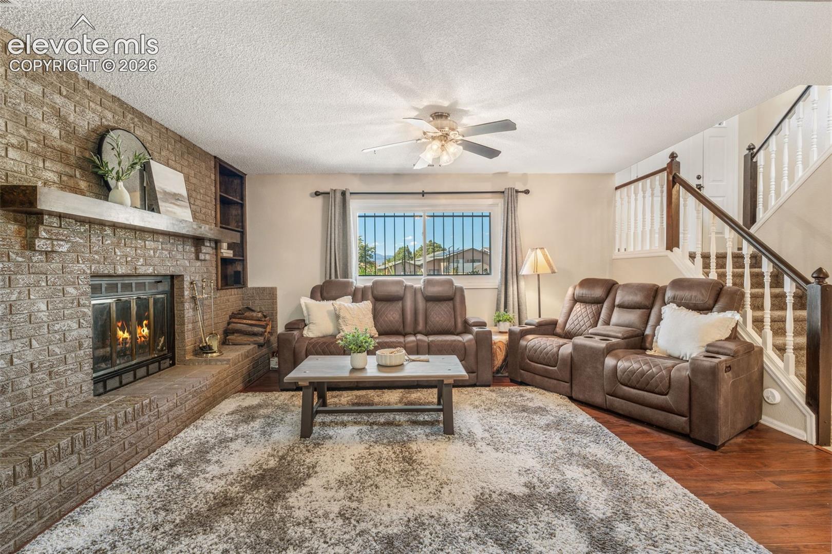 Full-height brick fireplace with a wood mantel, built-in shelving, wood-finish flooring, and a wooden staircase with a balustrade
