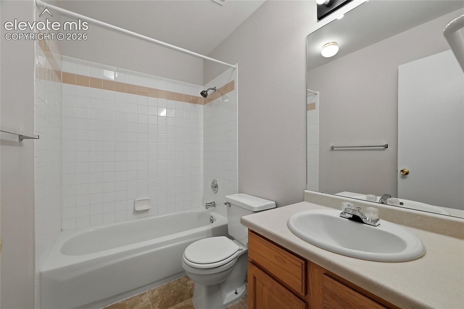 Full bathroom featuring a wood-finish vanity, solid-surface countertop with an integrated basin, wall-mounted mirror, and a tub-shower combination with ceramic tile surround