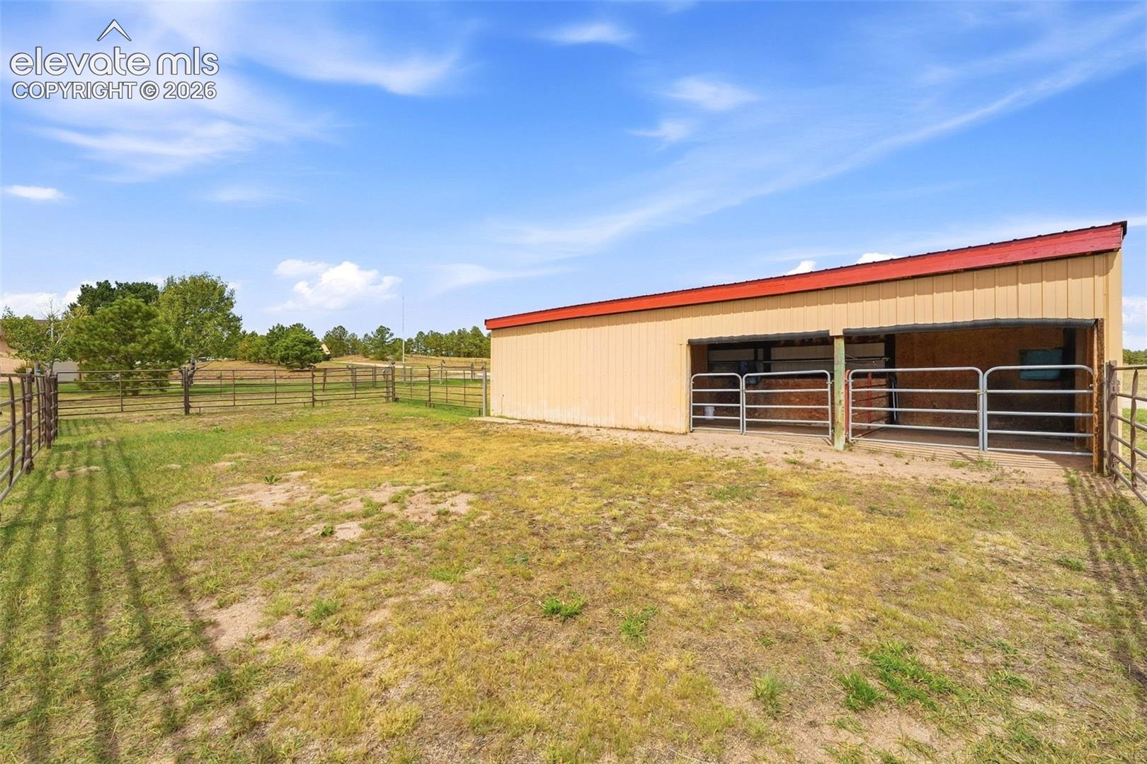 Metal outbuilding with a red sloped roof, two open stalls, and metal fencing