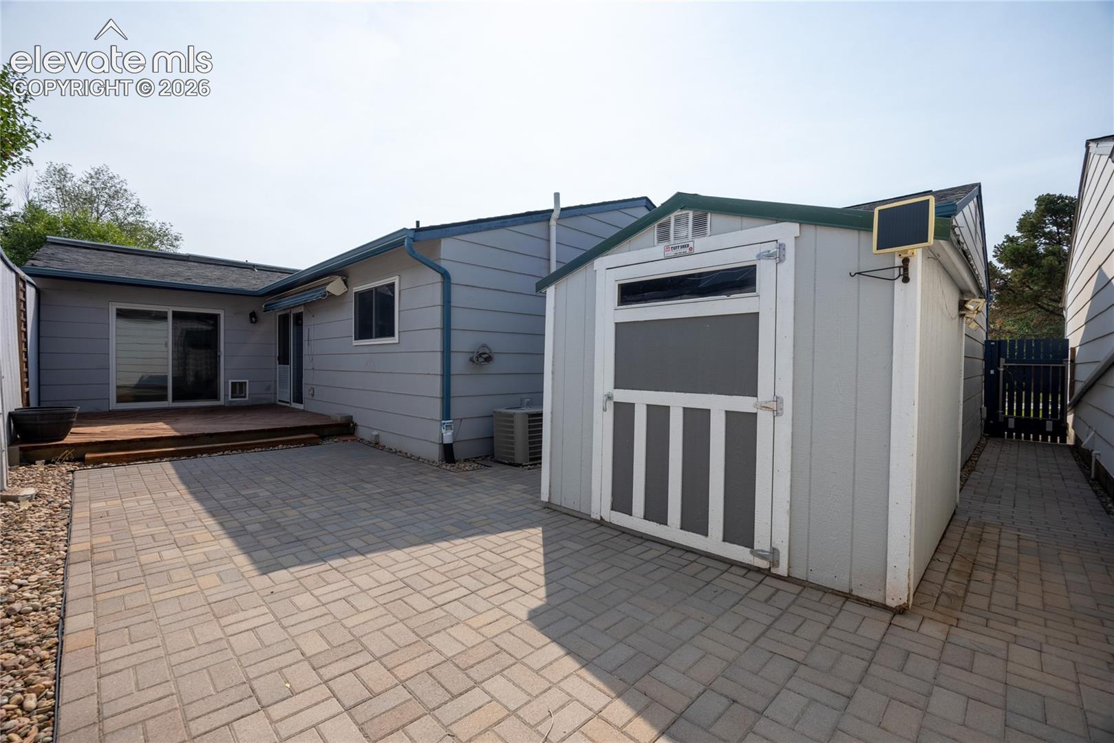 Rear exterior with a wood deck, paver patio, and detached storage shed