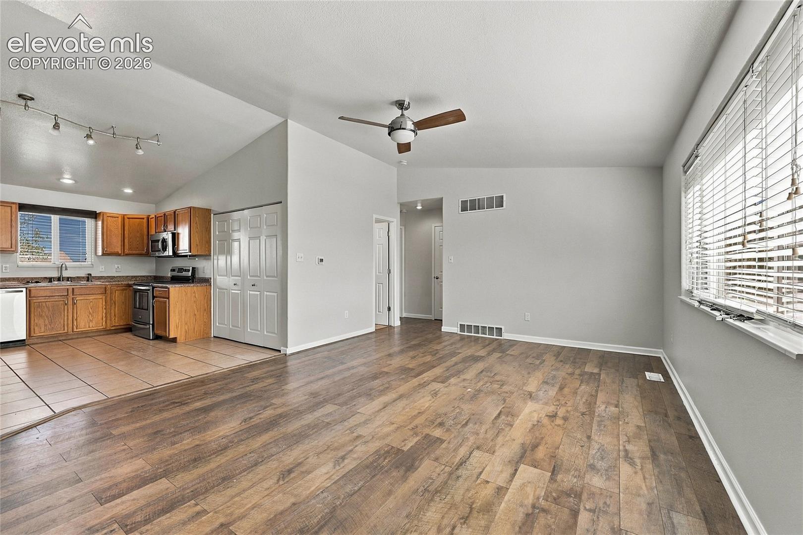 Vaulted ceilings featuring a central ceiling fan, wood-finish flooring, tile-surround kitchen flooring, wood cabinetry, and track lighting