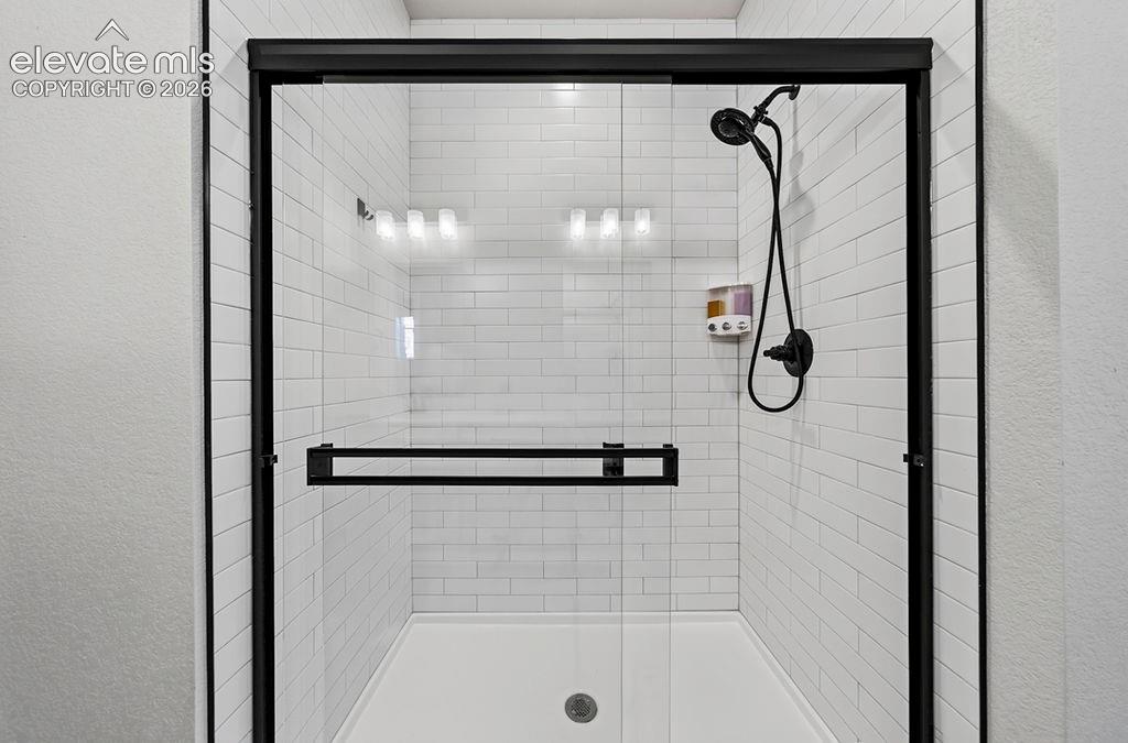 Walk-in shower featuring a sliding glass door with matte black framing, white subway tile surround, white shower pan, and a matte black shower head