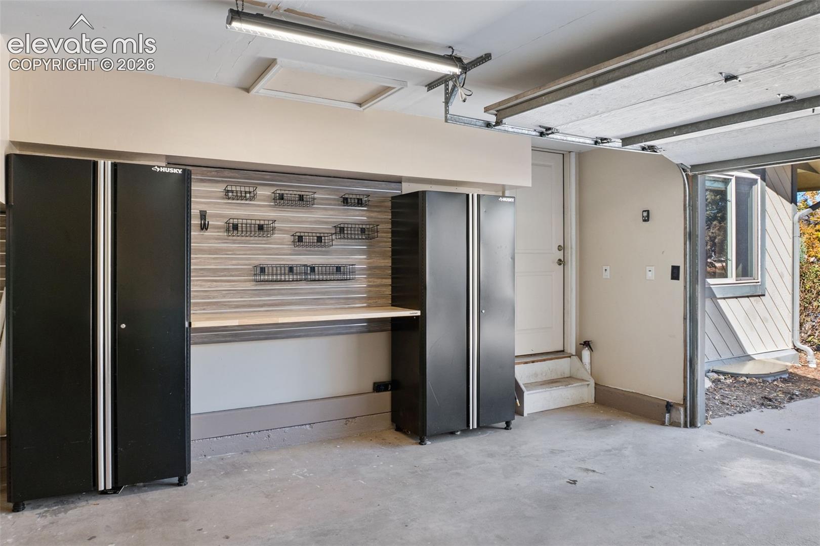 Garage featuring built-in cabinetry, integrated wall-mounted storage track system with metal shelving baskets, horizontal slat wall paneling, and an overhead LED fixture