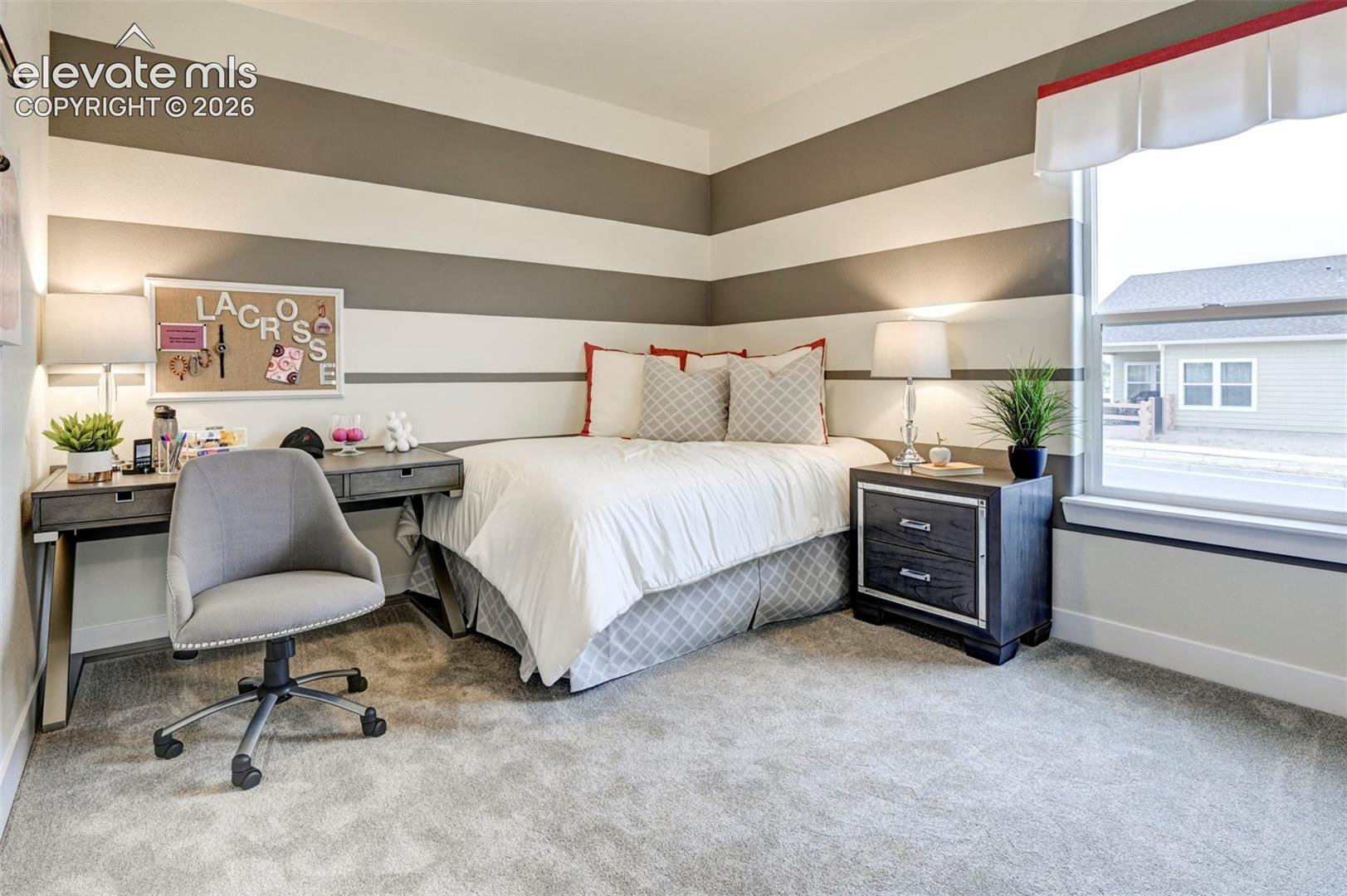 Striped accent wall, neutral carpet flooring, large window with trim, built-in desk, and a built-in nightstand