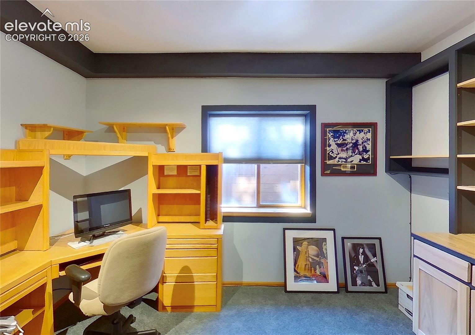 Built-in desk cabinetry, integrated shelving, and a single window with dark trim