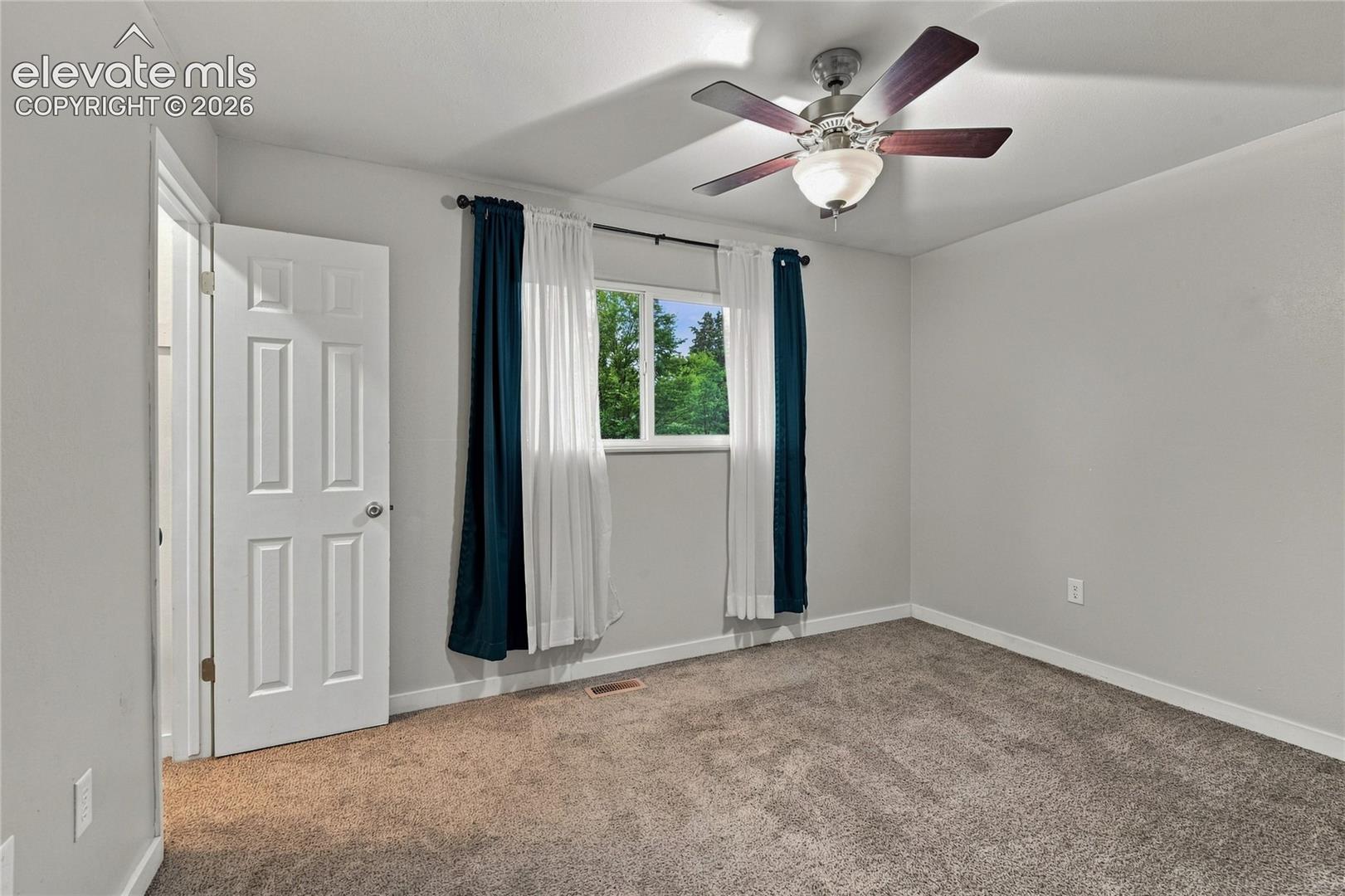 Spacious primary bedroom featuring walk-in closet, carpet flooring, a ceiling fan with integrated lighting, and large windows with dual-layer window treatments