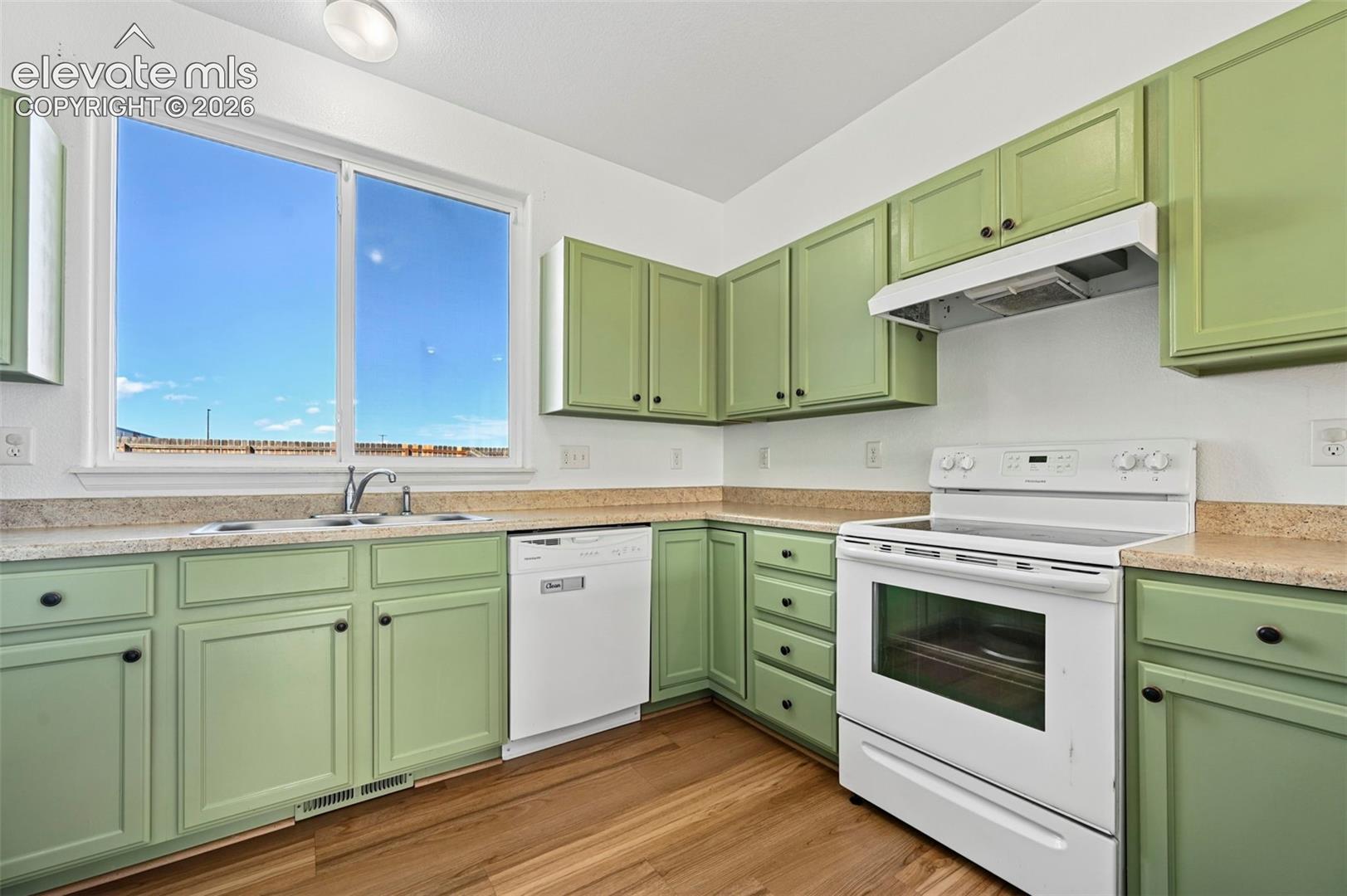 Kitchen featuring shaker-style cabinetry, solid-surface countertops, wood-finish flooring, a stainless steel sink with a goose-neck faucet, and a large window