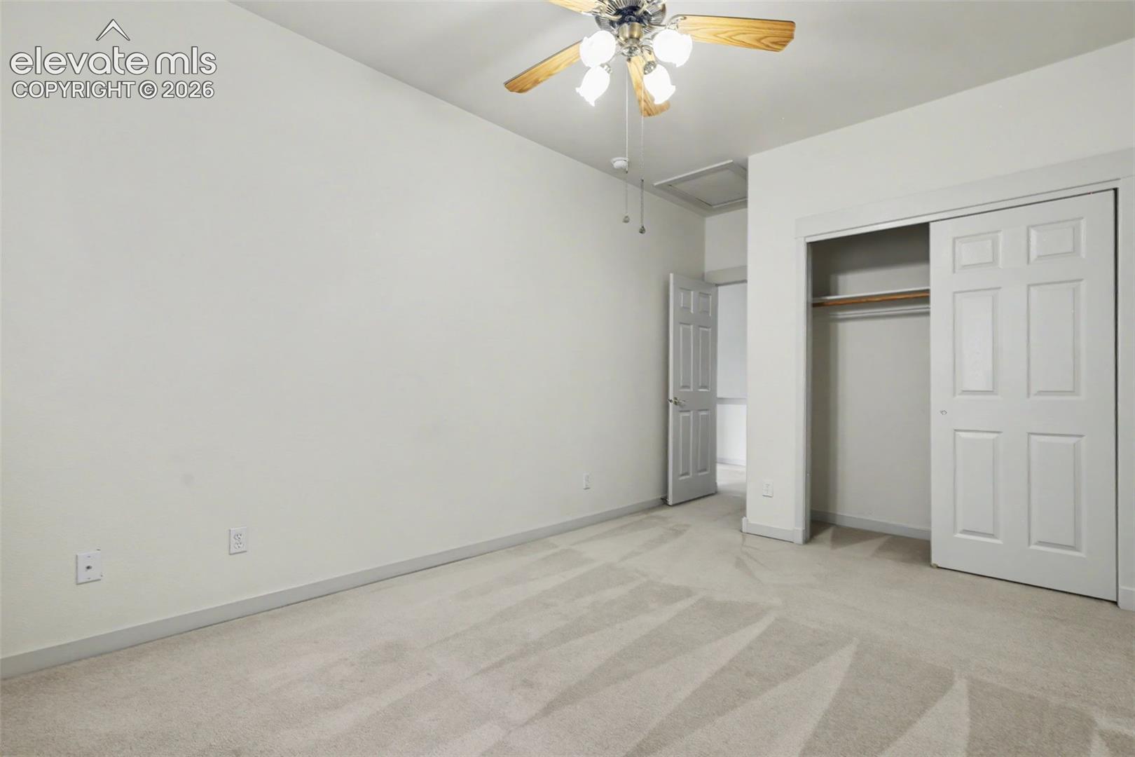 Carpeted room featuring a ceiling fan with light fixture, neutral wall paint, white trim, and a bi-fold closet with shelving and hanging rod