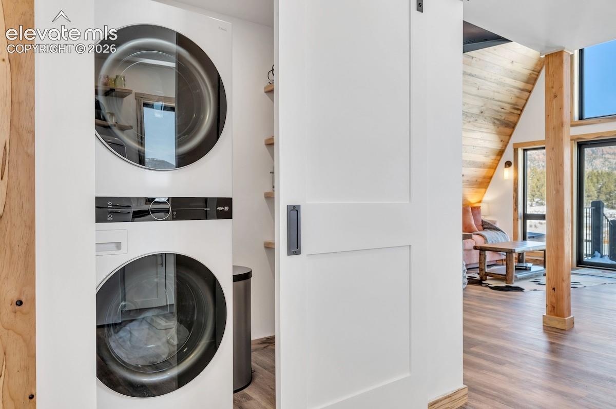 Laundry alcove featuring a stacked front-load washer and dryer, white sliding door with matte black hardware, and built-in wood shelving