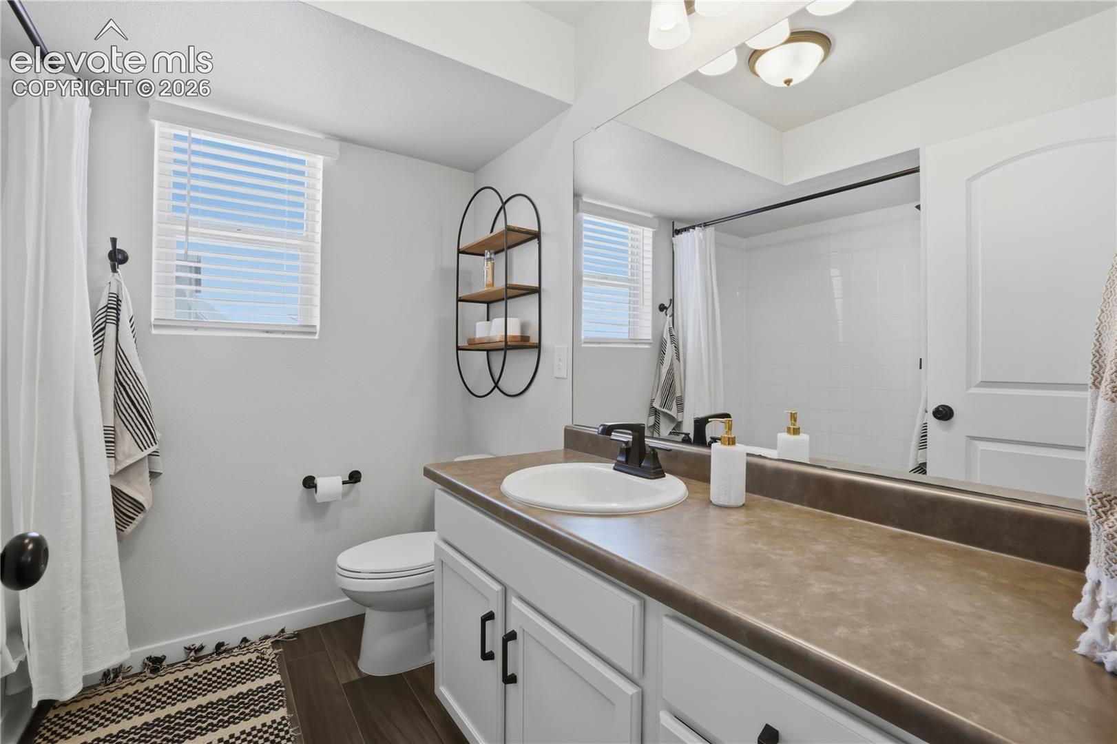Full bathroom featuring a single vanity with a white basin and dark countertop, white cabinetry with dark hardware, a large mirror, and a shower-tub combination with white subway tile surround