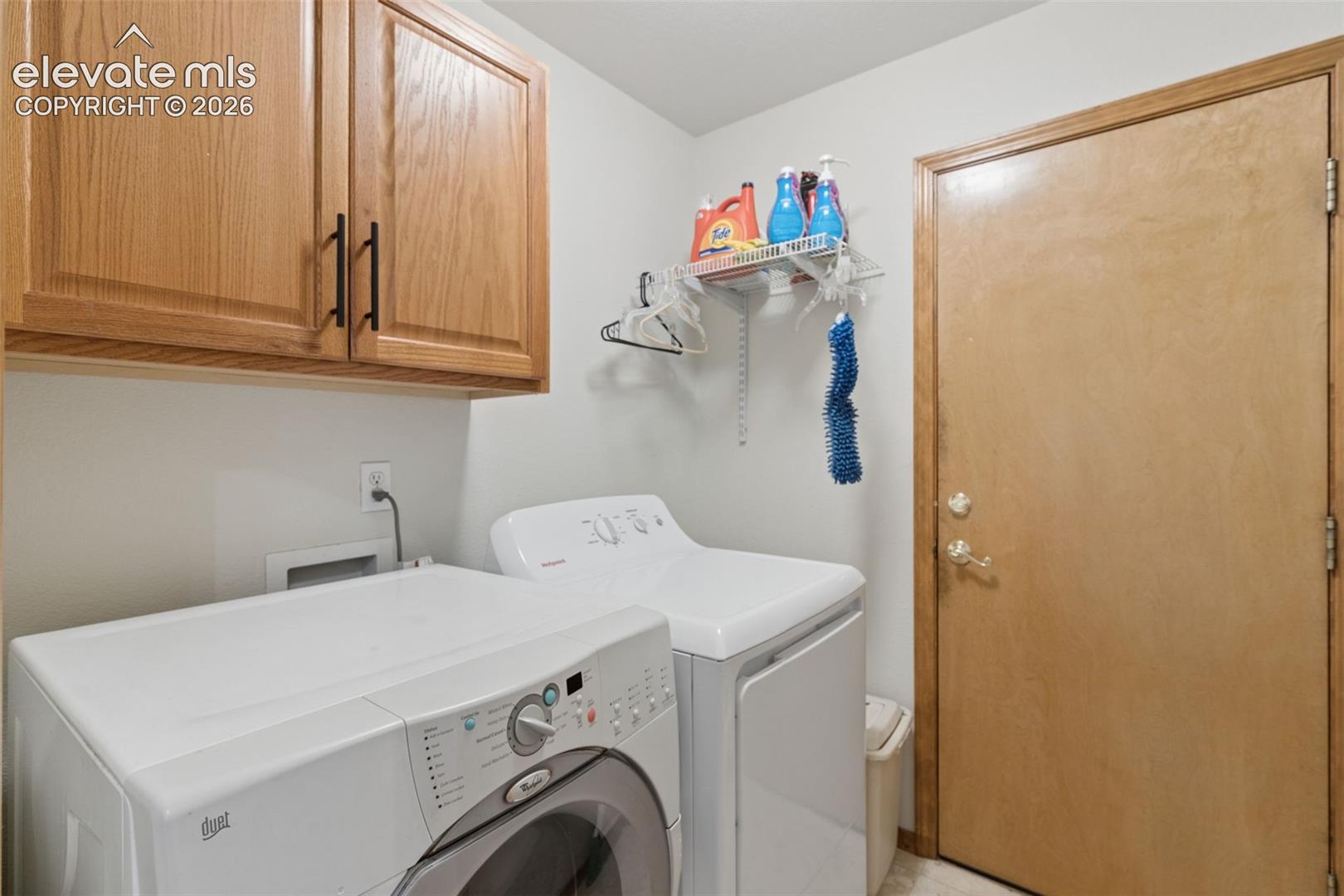 Utility room featuring stained wood cabinetry, a mounted wire shelf, and a solid wood door with metallic hardware