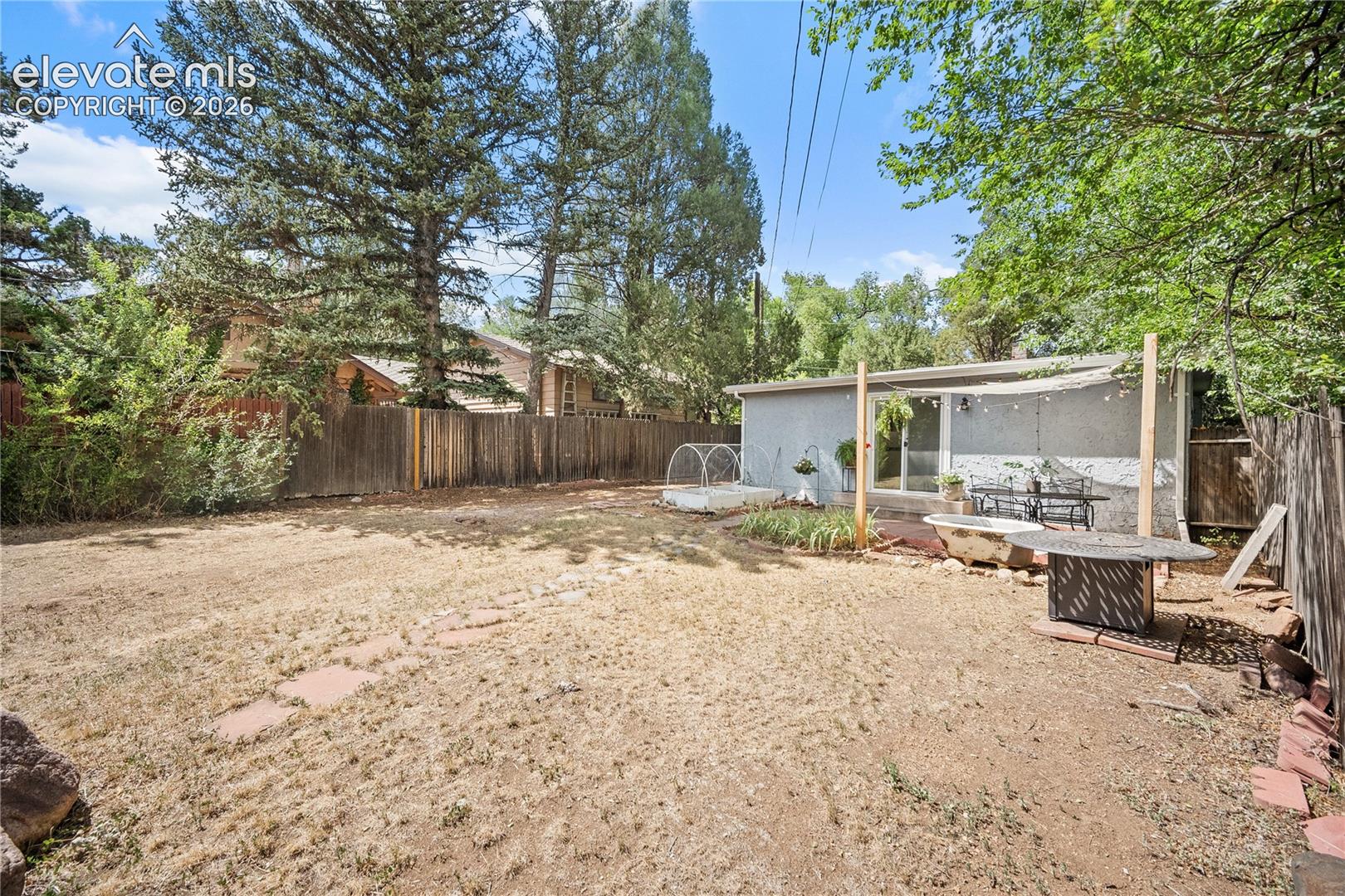 Expansive yard area featuring a detached structure with large windows, a covered patio space, and mature perimeter trees