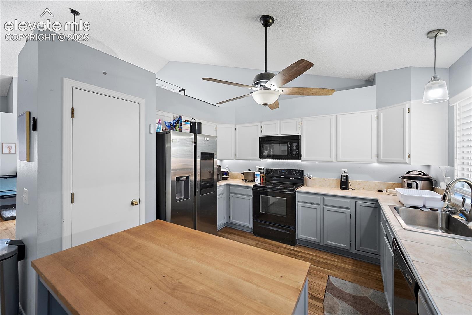Kitchen featuring white upper cabinetry, gray lower cabinetry, a stainless steel refrigerator, a black range, and a wood-finish island countertop