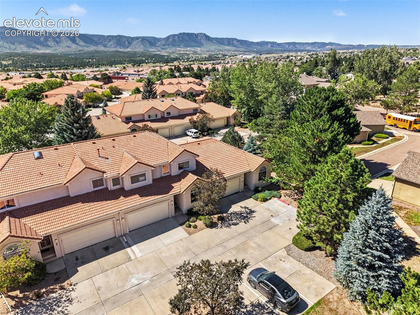 Terracotta tile roofing with multiple gables, mountain backdrop, mature evergreen trees, and a concrete driveway