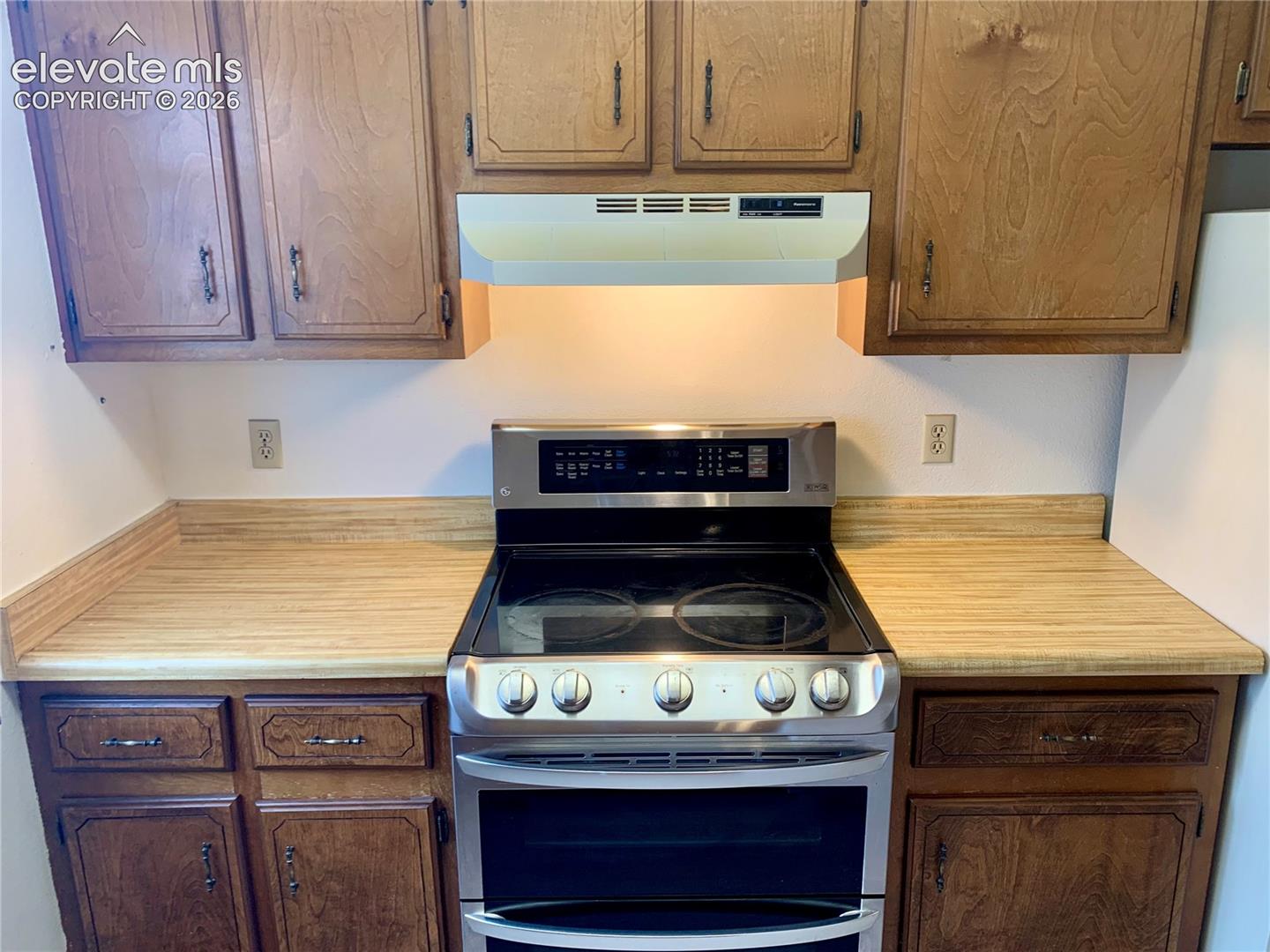 Stainless steel range with a glass cooktop, wood-finish countertops, wood upper cabinetry, and wood lower cabinetry