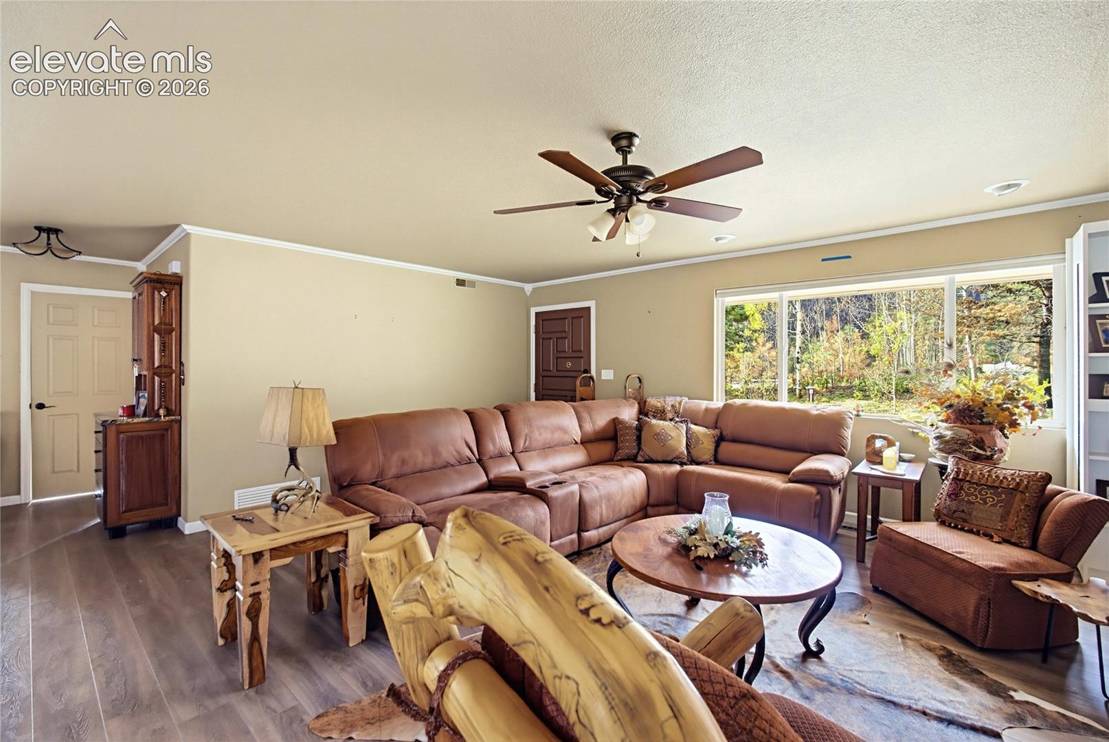 Neutral-toned interior featuring wood-finish flooring, a ceiling fan with integrated lighting, and a large picture window