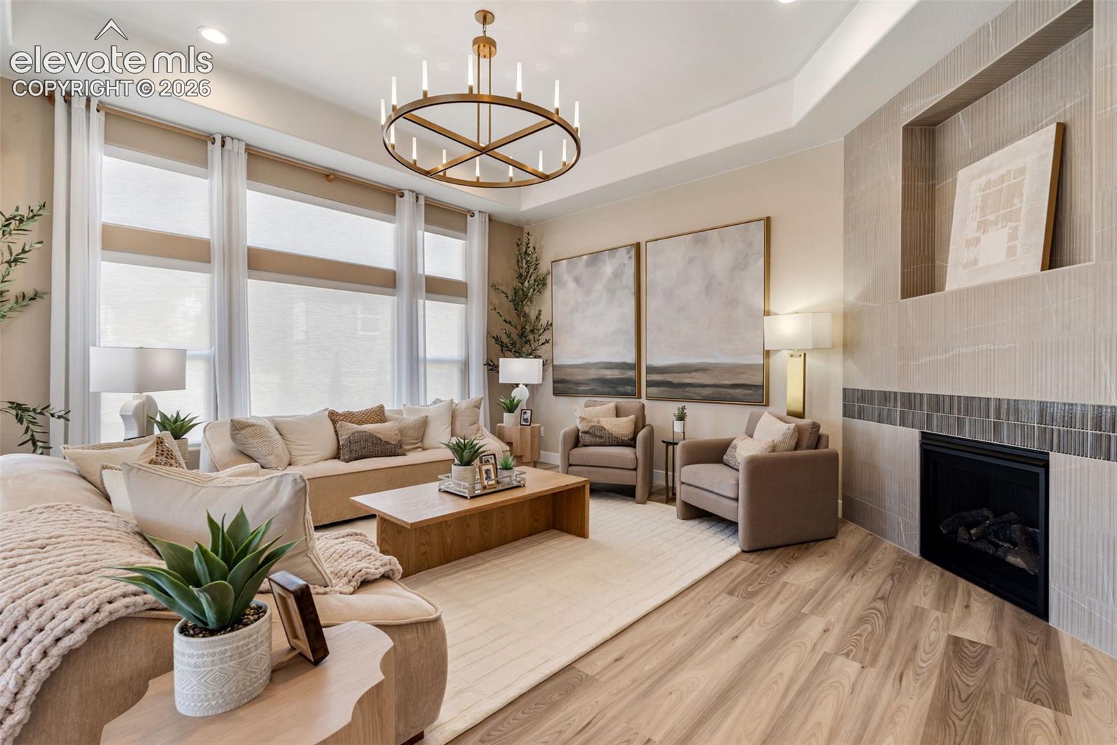 Living area featuring expansive windows, recessed tray ceiling, wood-finish flooring, and a floor-to-ceiling fireplace with built-in niche