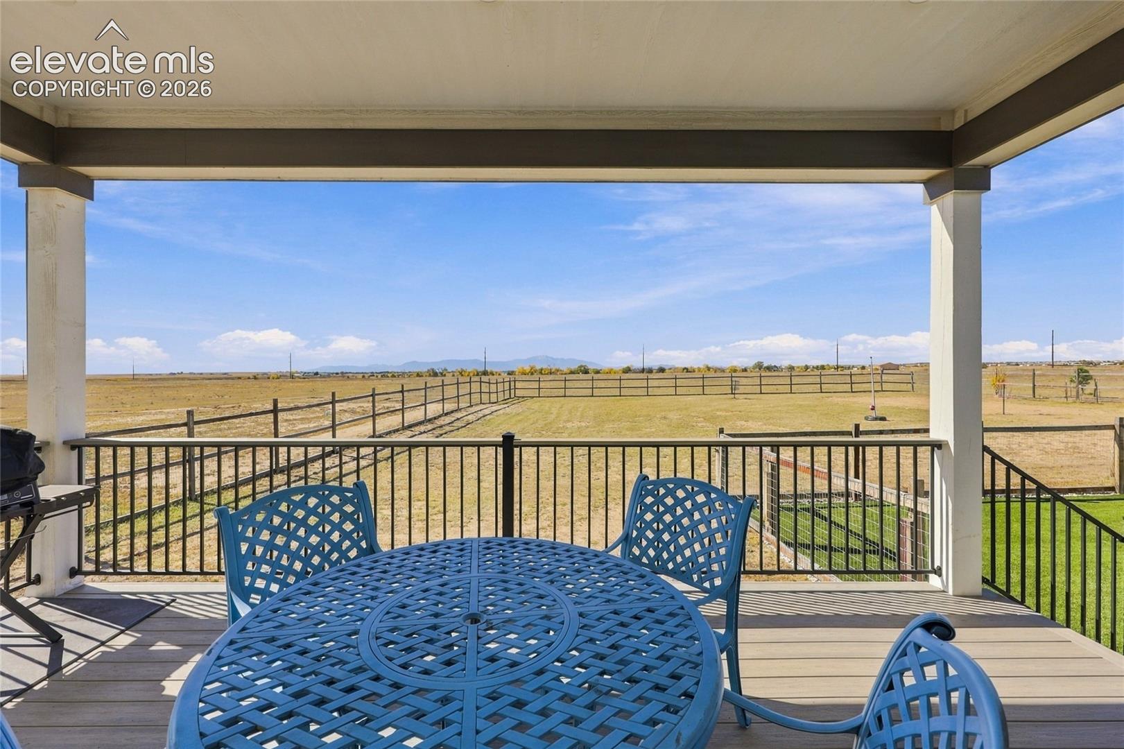 Covered patio featuring composite decking, black metal railing, and an expansive exterior landscape with mountain silhouettes