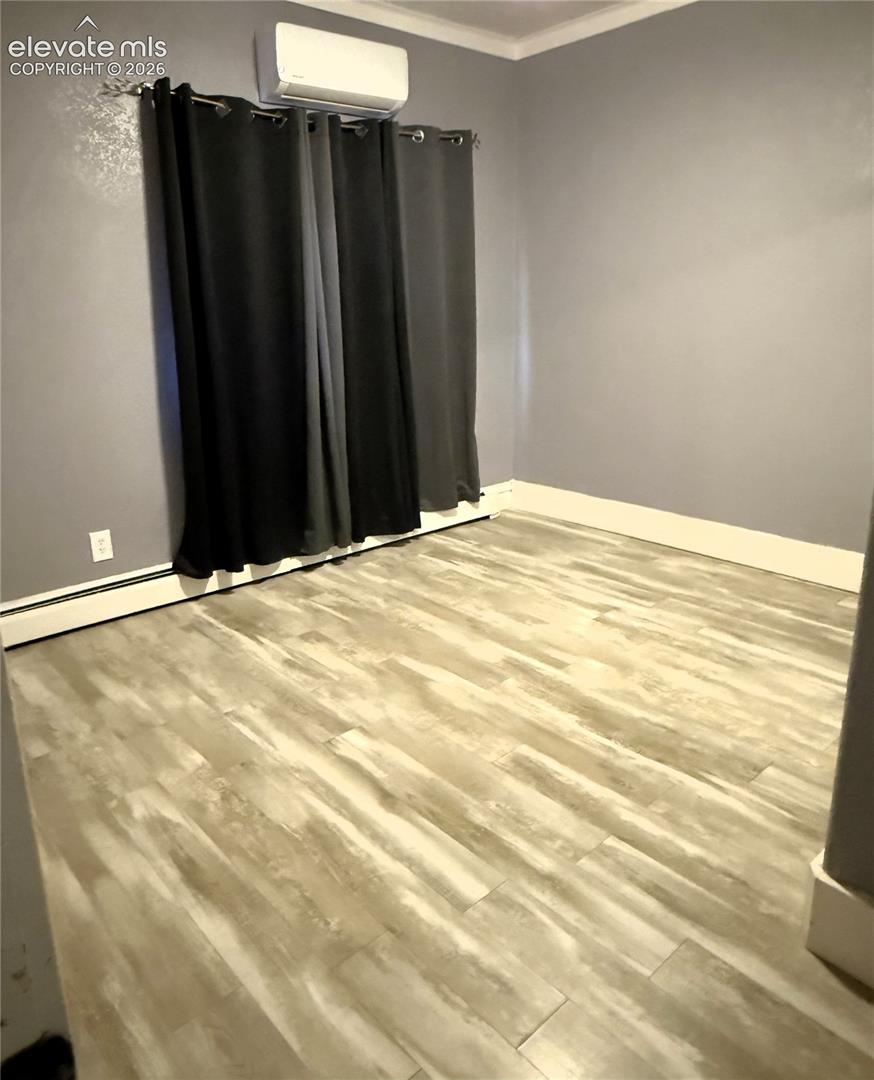 Room featuring wood-finish flooring, neutral wall paint, and a wall-mounted ductless heating and cooling unit