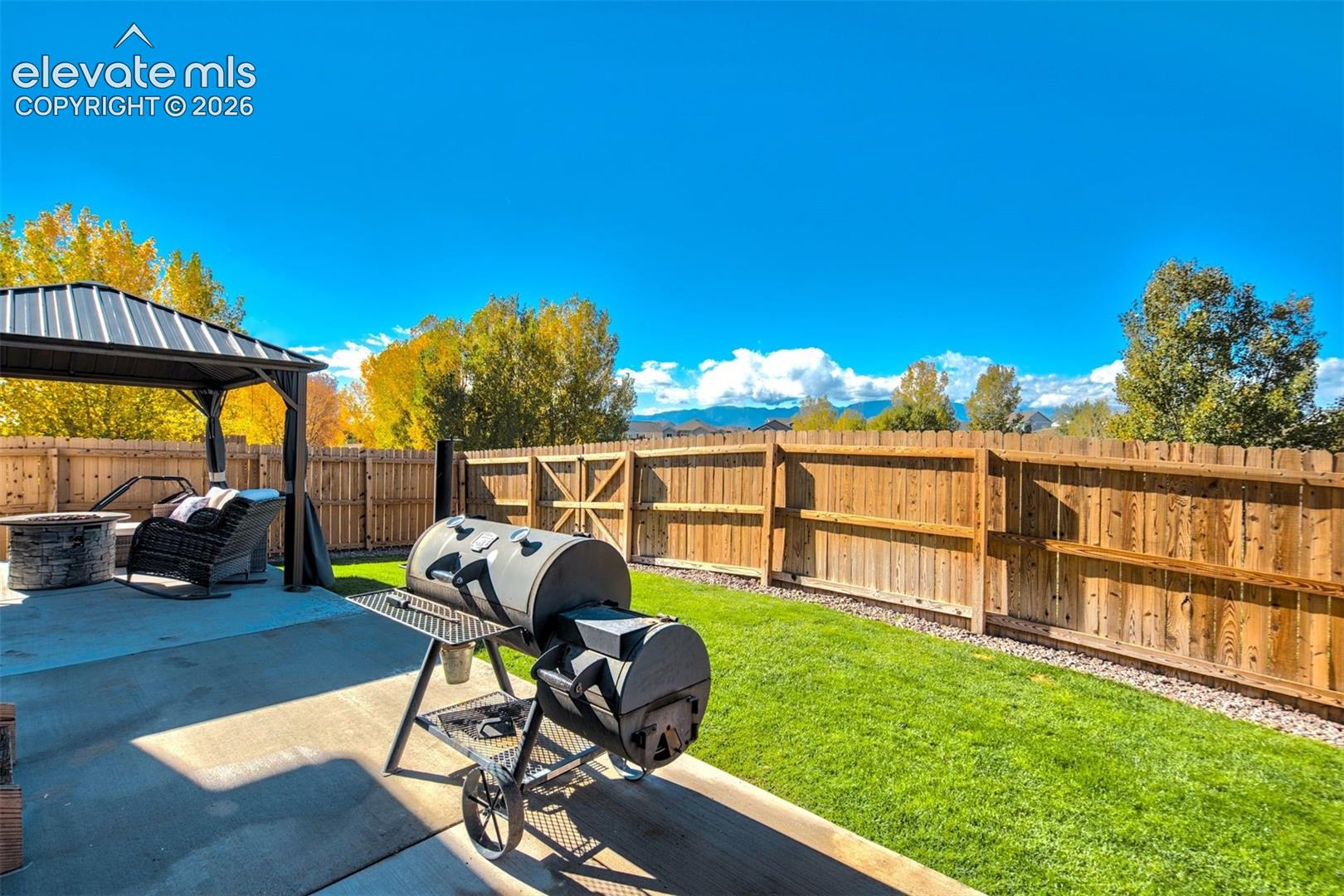 Backyard featuring a concrete patio, wood privacy fencing, metal gazebo, and mountain backdrop