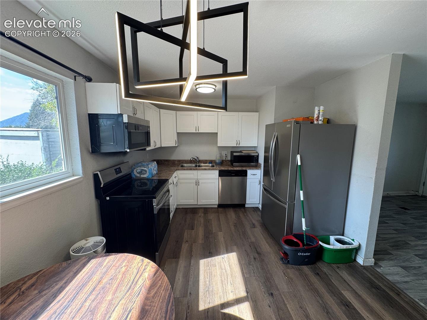 Kitchen featuring wood-finish flooring, white cabinetry, integrated stainless steel dishwasher, stainless steel refrigerator, and a modern geometric pendant light fixture