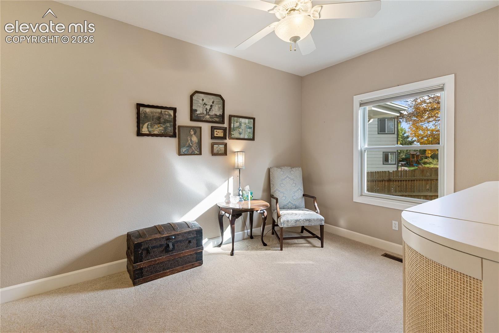 Neutral tone walls, white trim, window with natural light, textured carpet flooring, and a ceiling fan with integrated lighting