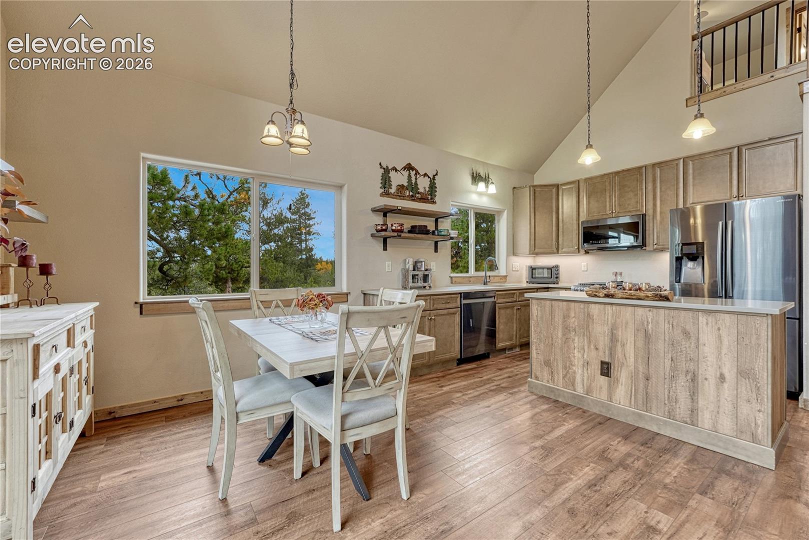 Vaulted ceilings, wood-finish flooring, central kitchen island with cabinetry base, stainless steel appliances, and wood-toned cabinetry