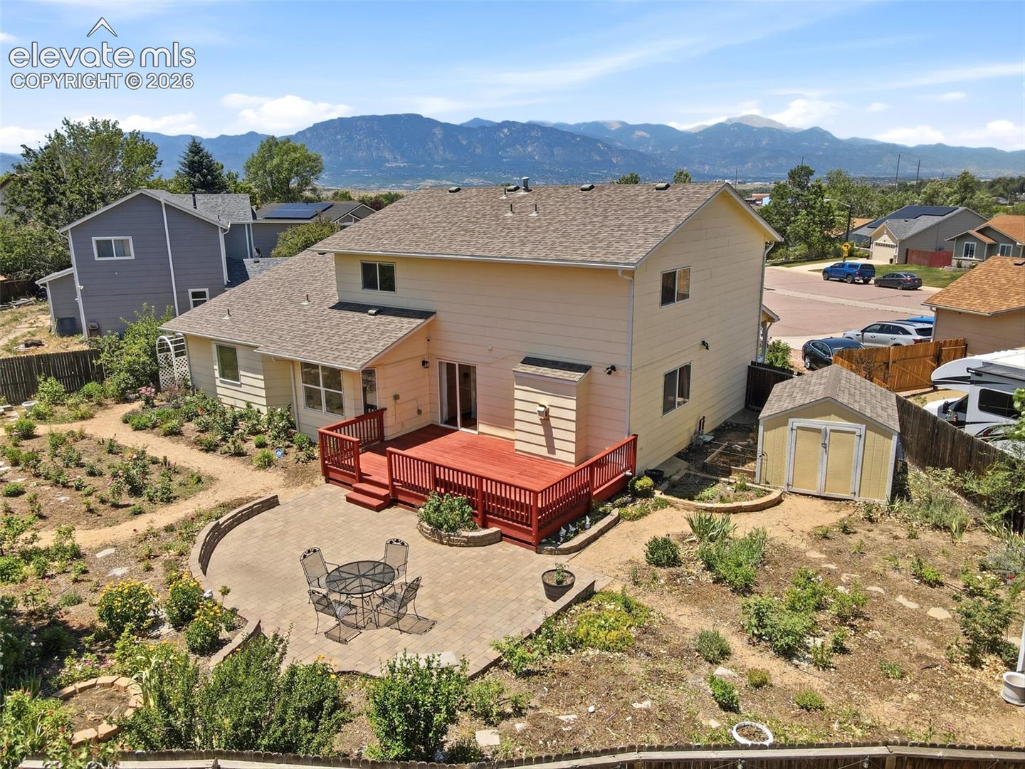 Expansive backyard featuring a red wood-finish deck, a semicircular paver patio, and a dedicated storage shed