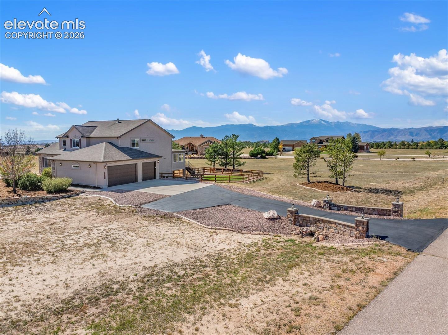 Two-story residence featuring a multi-car garage, expansive acreage, stone-accented gated driveway entrance, and mountain scenery
