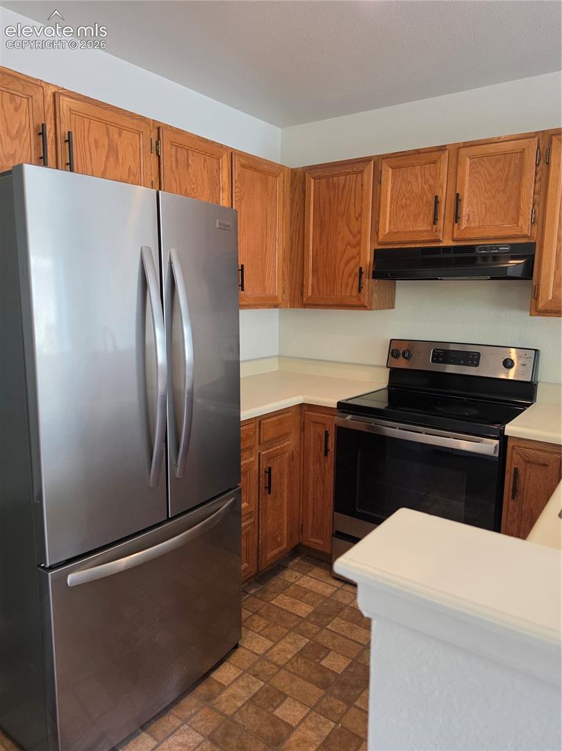 Kitchen featuring wood cabinetry, stainless steel French-door refrigerator, electric range with black cooktop, range hood, and solid-surface countertops