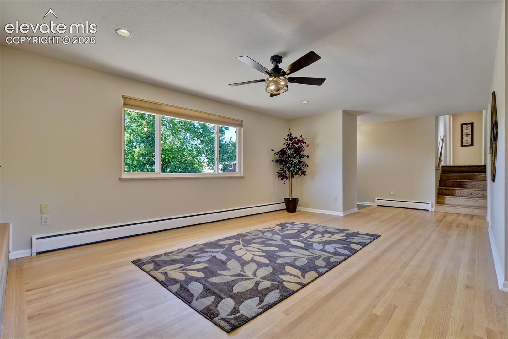 Neutral-toned living space featuring light wood-finish flooring, a ceiling fan with integrated light fixture, and recessed lighting