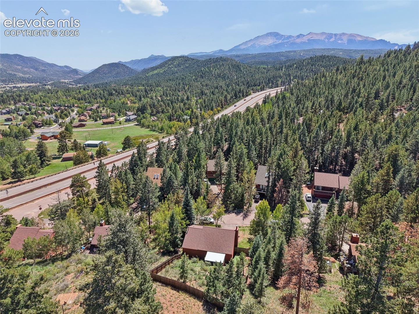 Aerial perspective showcasing a mountainous backdrop, extensive evergreen tree coverage, and community roads