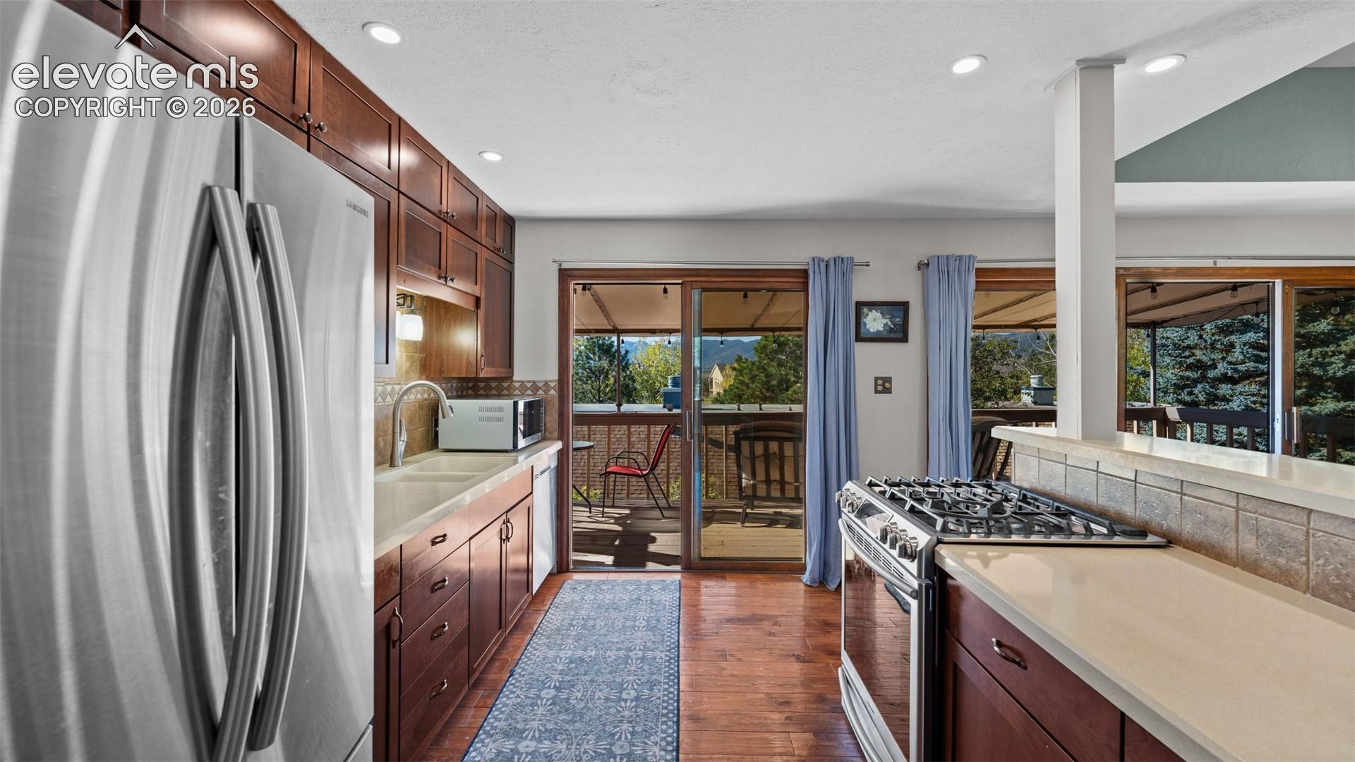 Kitchen featuring dark wood cabinetry, solid-surface countertops, built-in stainless steel appliances, wood-finish flooring, and sliding glass doors