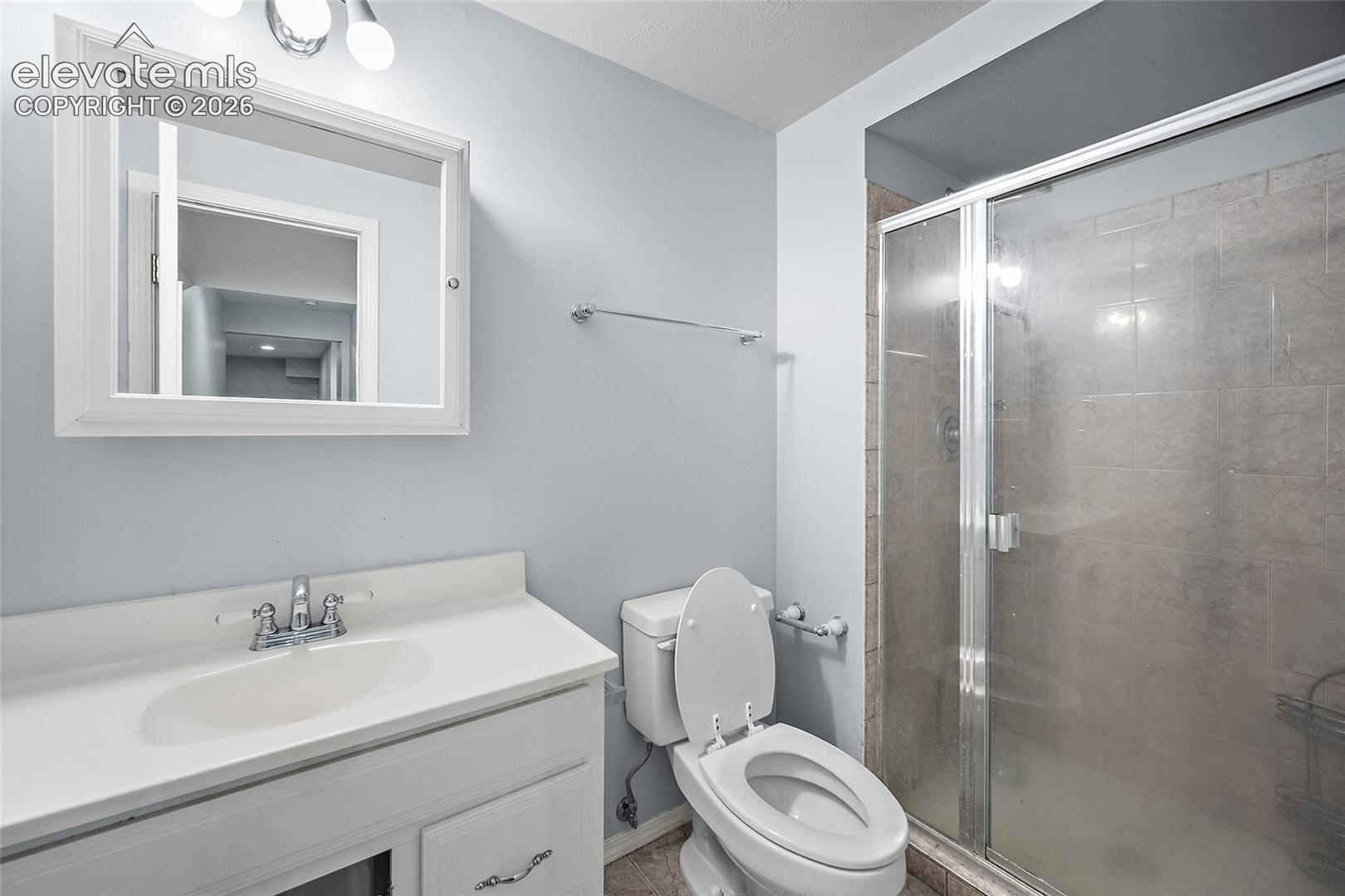 Vanity with integrated sink, chrome faucet, white medicine cabinet, and glass-enclosed shower with tiled walls
