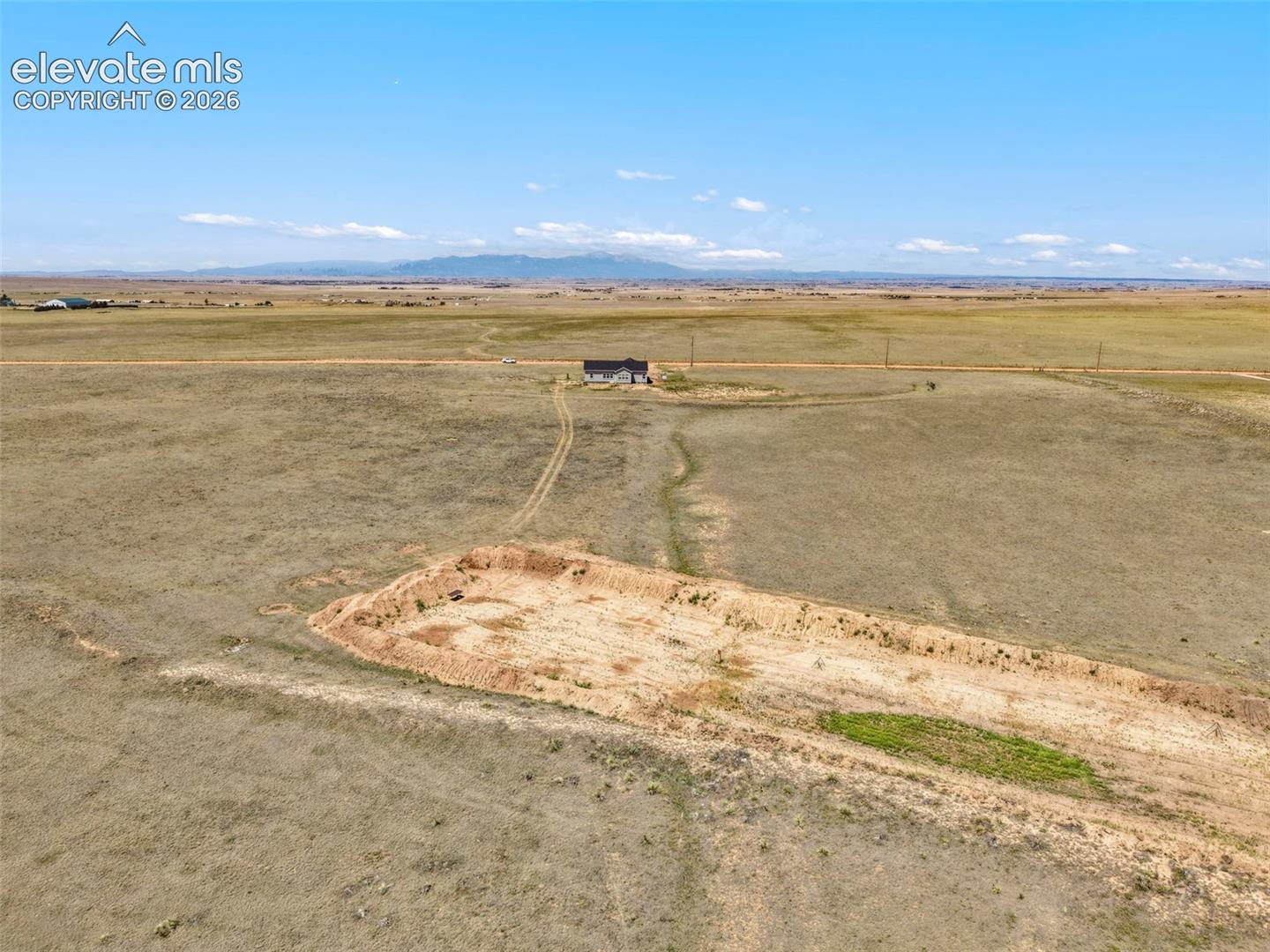 Expansive land parcel featuring a distant single-family residence, a cleared building area, and a flat topography