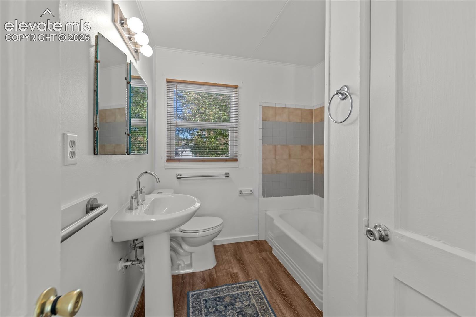 Bathroom featuring a porcelain pedestal sink, wood-finish flooring, and a tub with horizontal tile surround