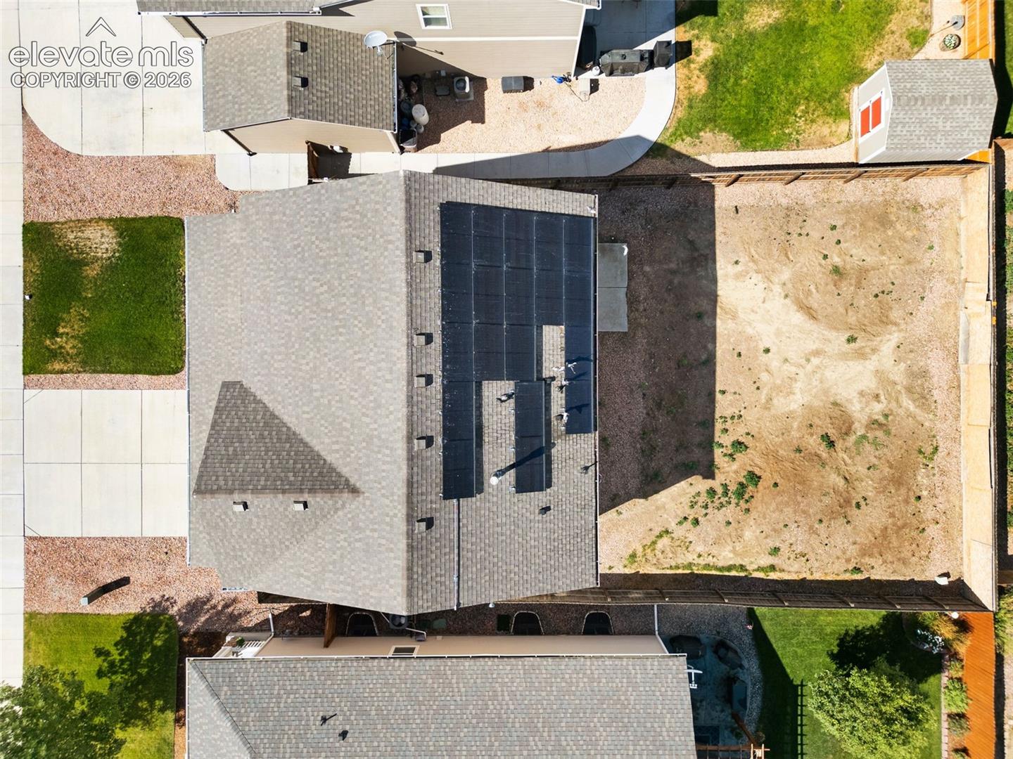 Aerial view featuring a roof-mounted solar panel system, asphalt shingle roofing, a concrete driveway, and a fenced-in yard