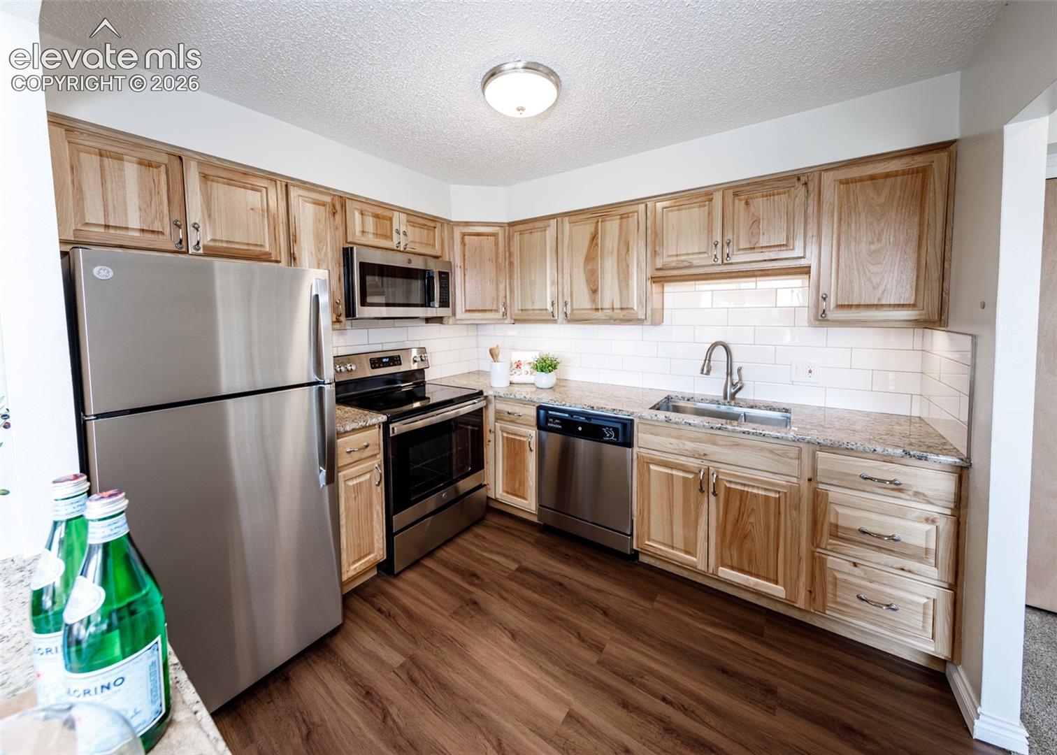Kitchen featuring natural-finish wood cabinetry, stainless steel appliances, stone-surface countertops, white subway tile backsplash, and wood-finish flooring