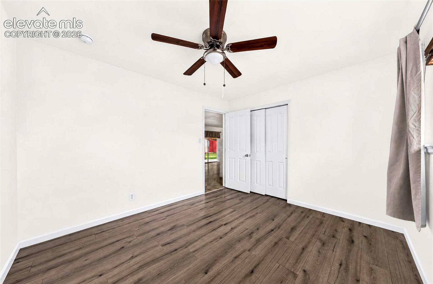 Room featuring wood-finish flooring, a central ceiling fan with integrated lighting, and white six-panel closet doors