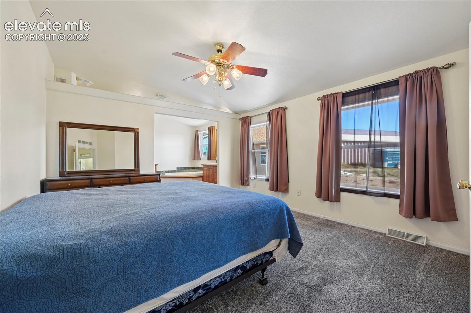 Bedroom featuring a vaulted ceiling with a four-light brass finish ceiling fan, wall-to-wall carpeting, and windows with neutral drapery