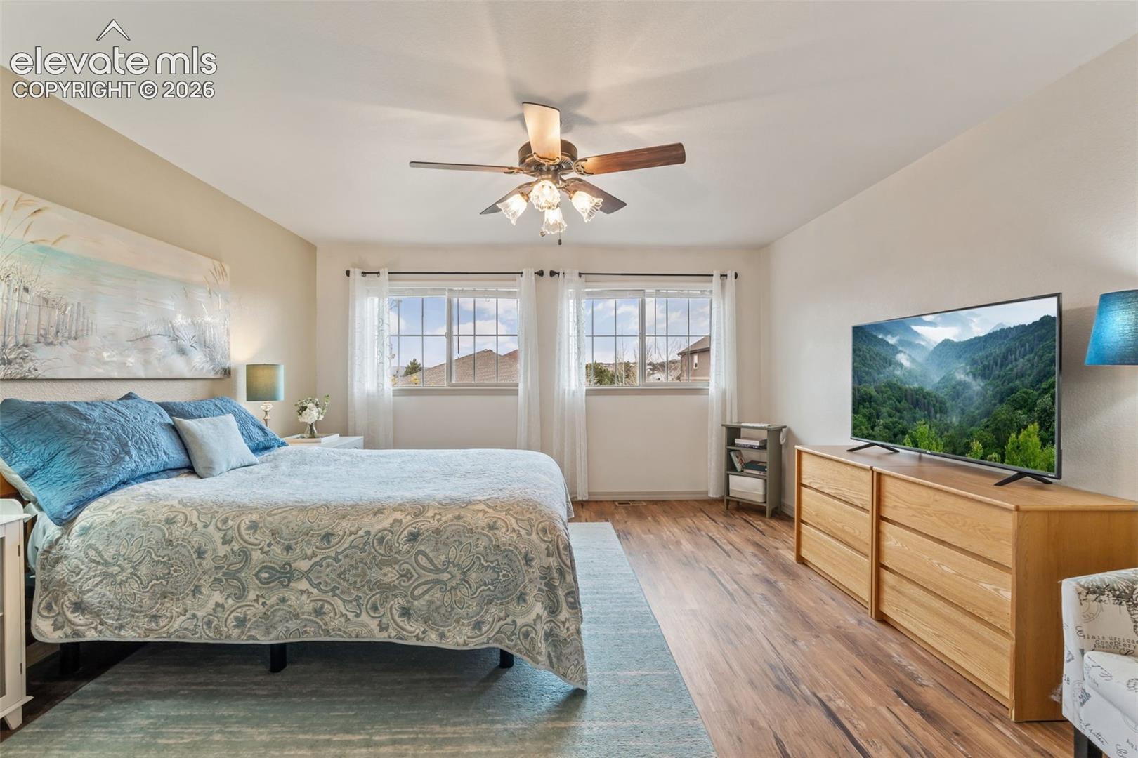 Room with wood-finish flooring, two large windows with white trim, and a ceiling fan with integrated lighting