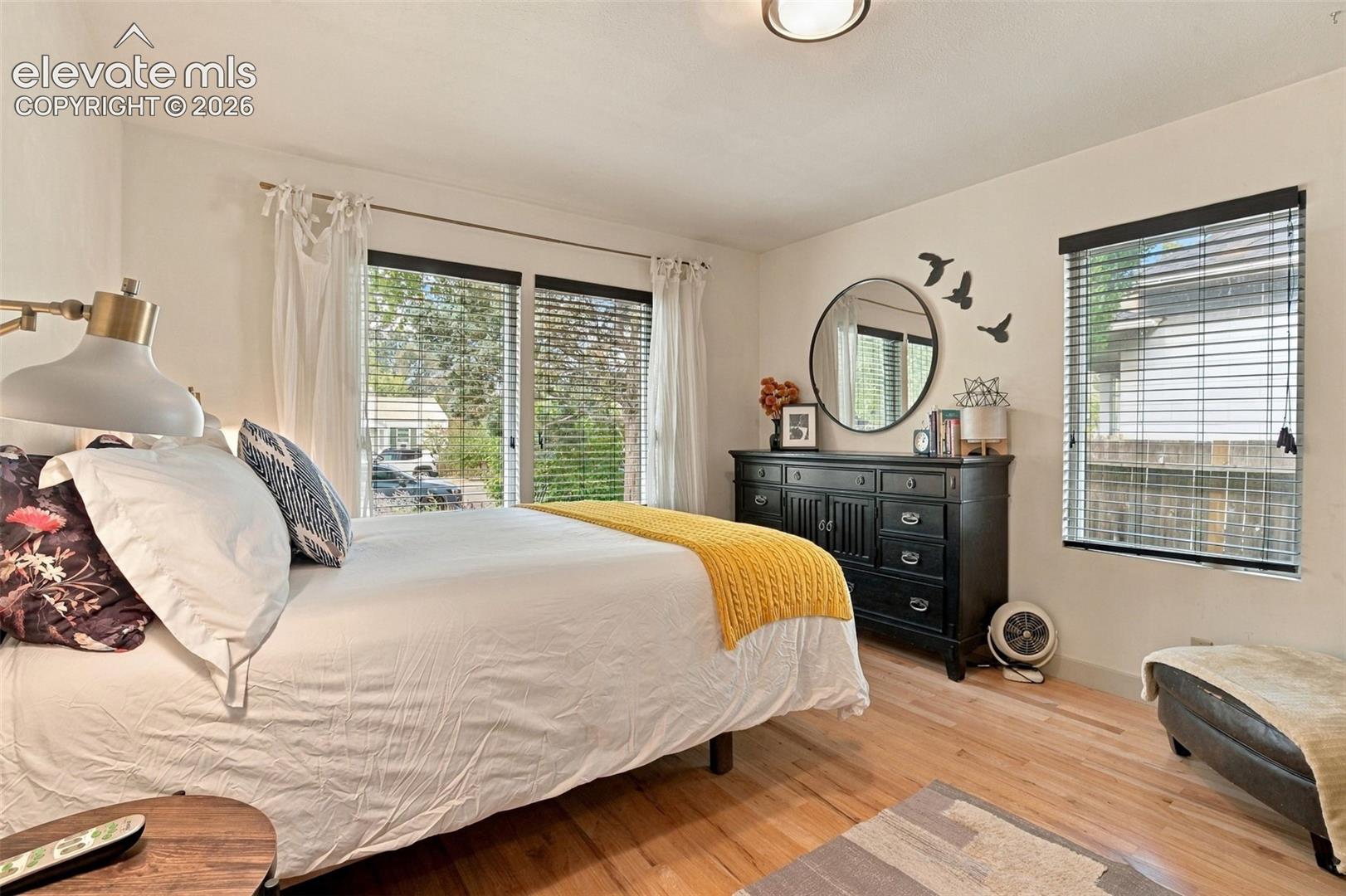 Room featuring wood-finish flooring, dual windows with horizontal blinds, and a central ceiling light fixture