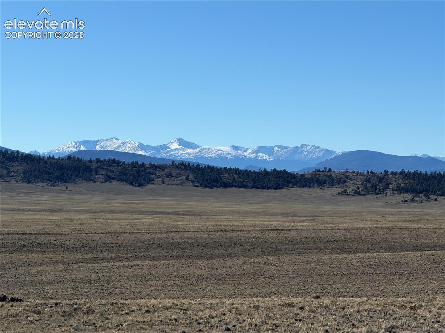 Expansive terrain featuring snow-capped mountain backdrops and native grasses