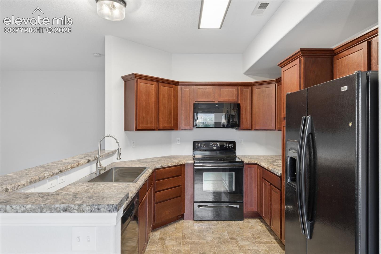 Kitchen featuring rich wood cabinetry, stone-finish countertops, stainless steel sink with a high-arch faucet, black built-in appliances, and resilient tile flooring