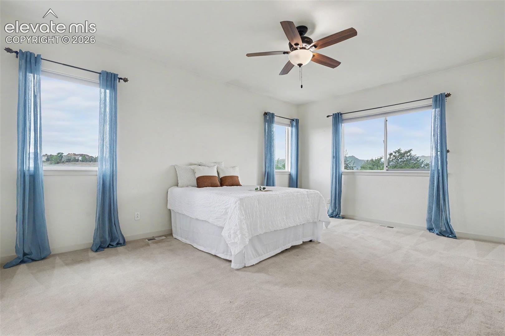 Carpeted room featuring multiple windows with natural light, a ceiling fan with integrated lighting, and white painted walls