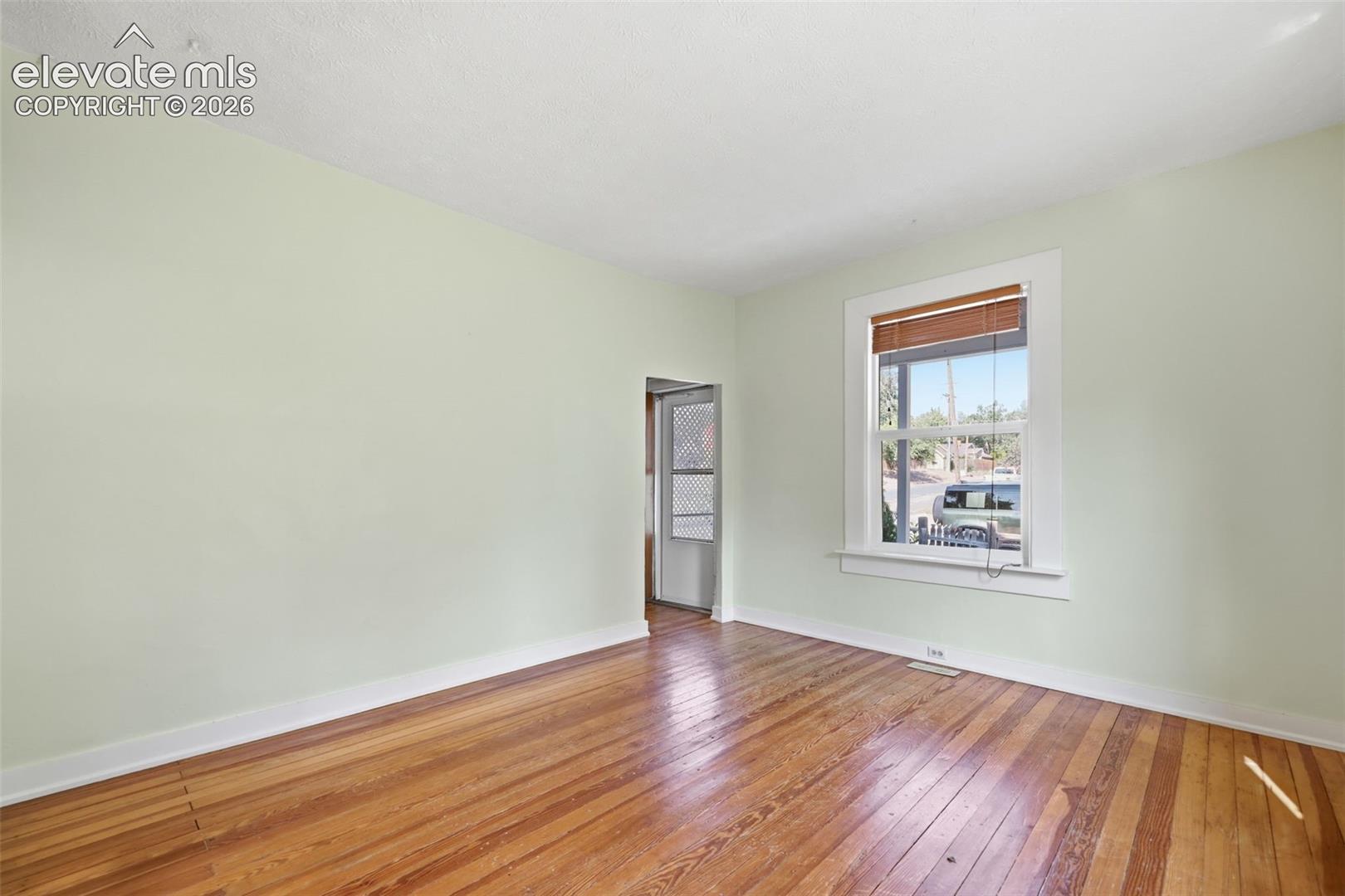 Living room with pine hardwood flooring, painted walls, window with wooden blinds, and white trim.