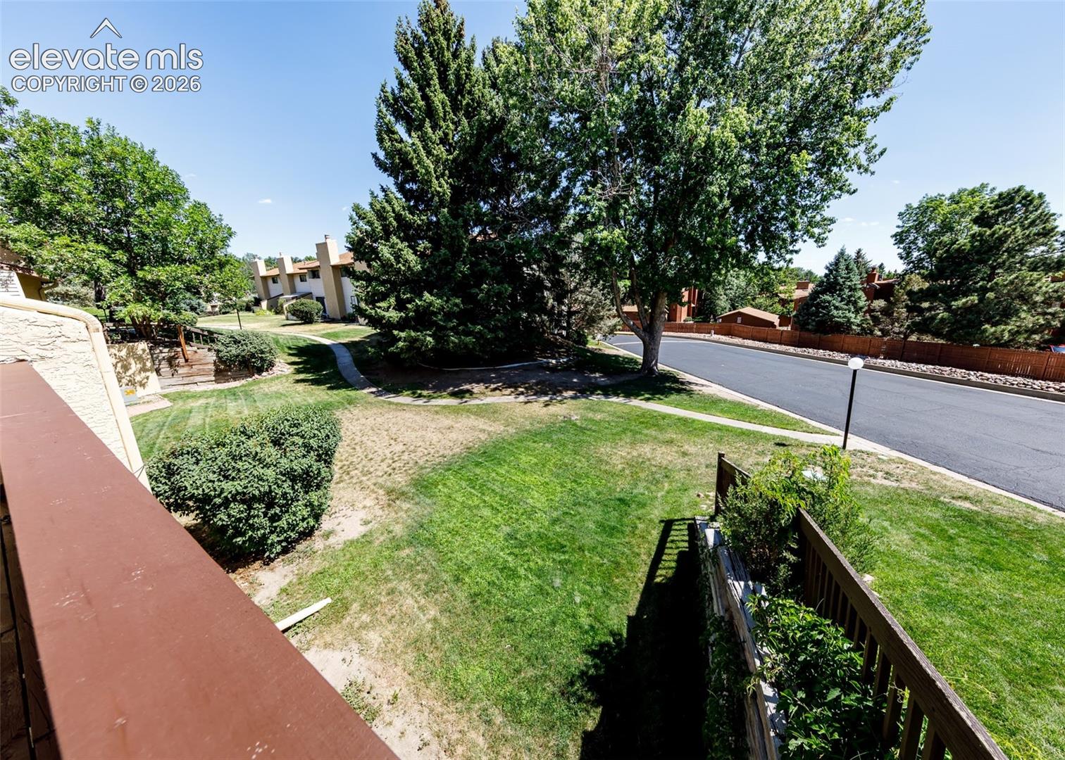Exterior balcony featuring a solid wood railing overlooking a lawn area with mature evergreen and deciduous trees