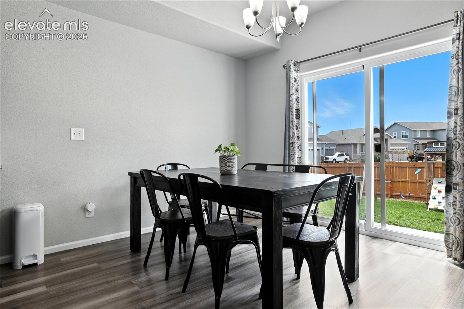 Sliding glass door, wood-finish flooring, overhead chandelier, light-toned walls, and a private fenced backyard